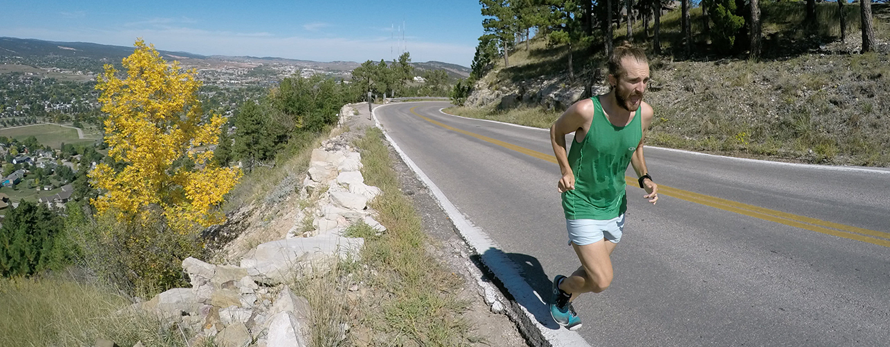 coureur homme court en côte sur une route bitumée en montagne