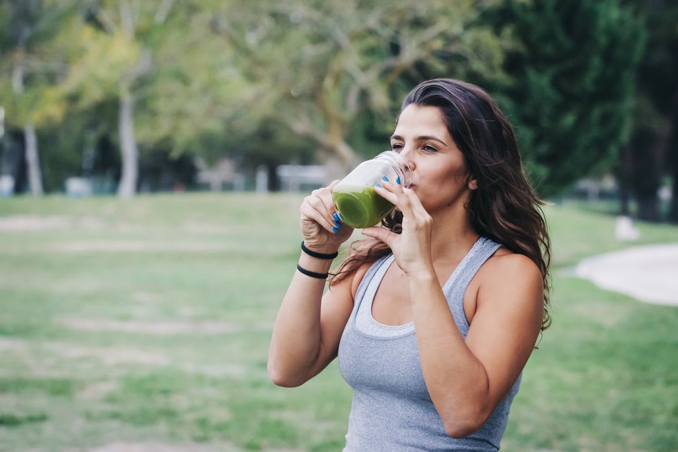 Une femme sportive boit un verre d'eau à la chlorophylle