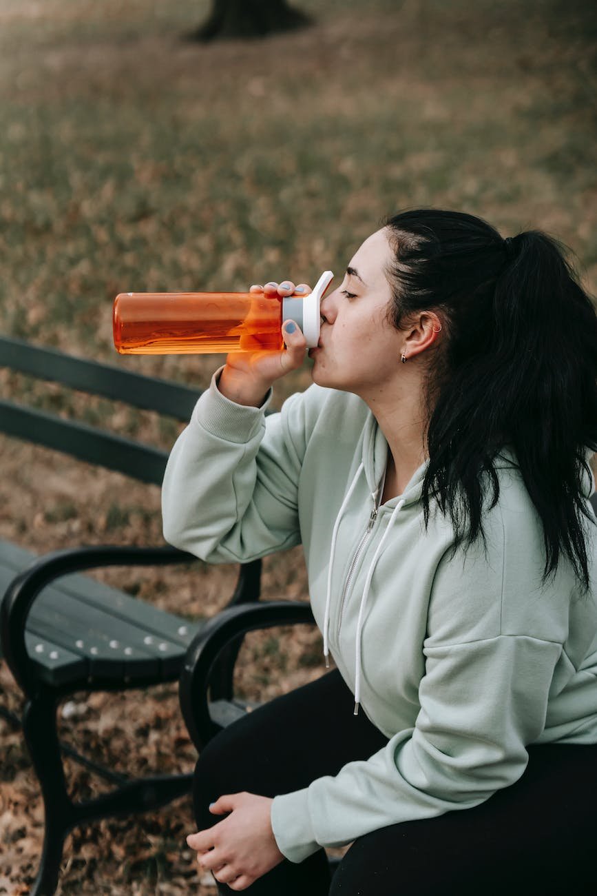 joggeuse buvant de l'eau sur un banc dans un parc d'automne