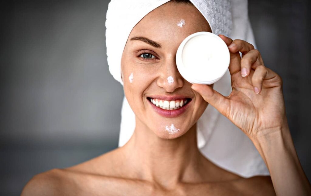 Une femme souriante hydrate la peau de son visage
