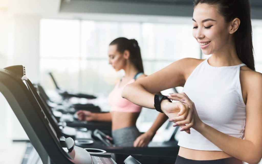 2 coureuses courent sur un tapis de course et 1 regarde sa montre GPS