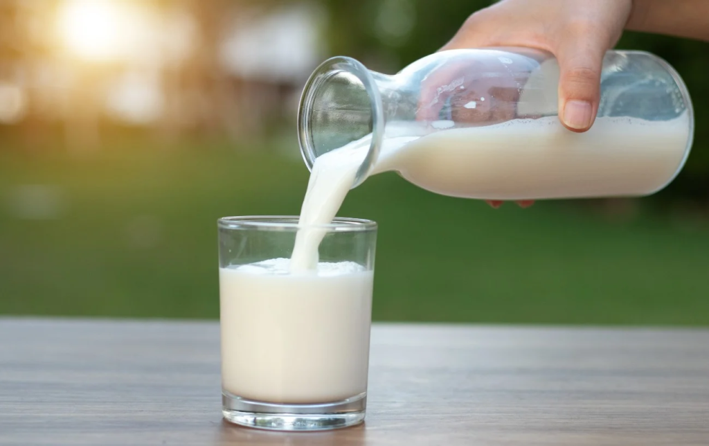 Une personne remplit un verre de lait avec une carafe