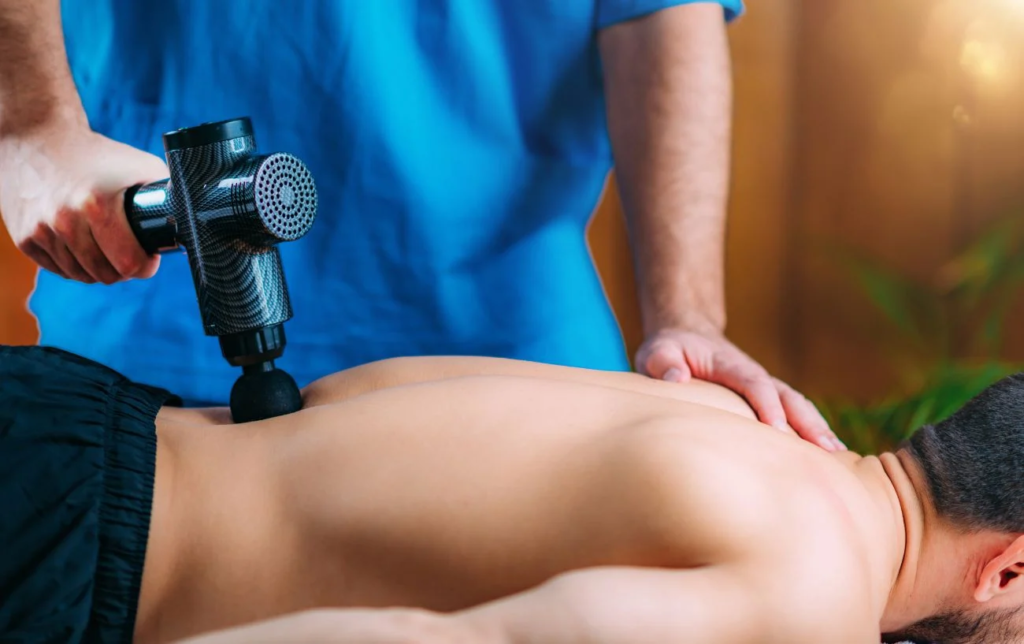 Un kiné utilise un pistolet de massage sur le dos d'un patient