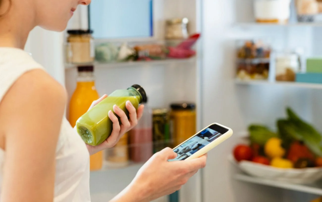 Une femme regarde son smartphone avec un smoothie en bouteille