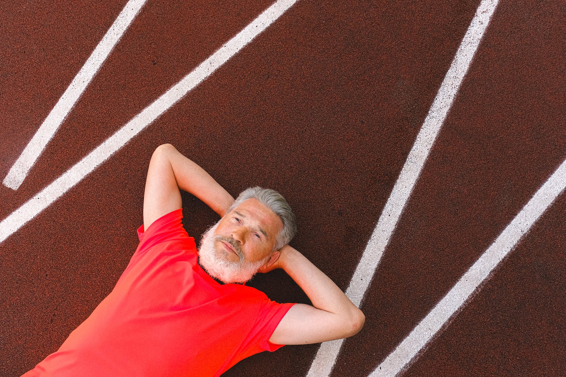 homme âgé avec barbe se reposant paisiblement sur une piste d'athlétisme