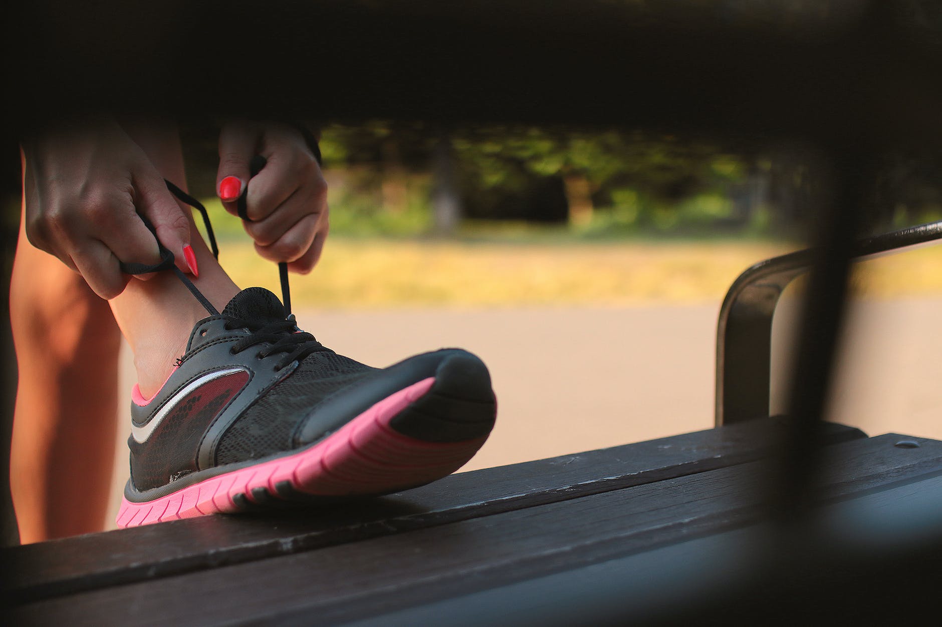 woman in black and pink sneaker tying lace of her shoe