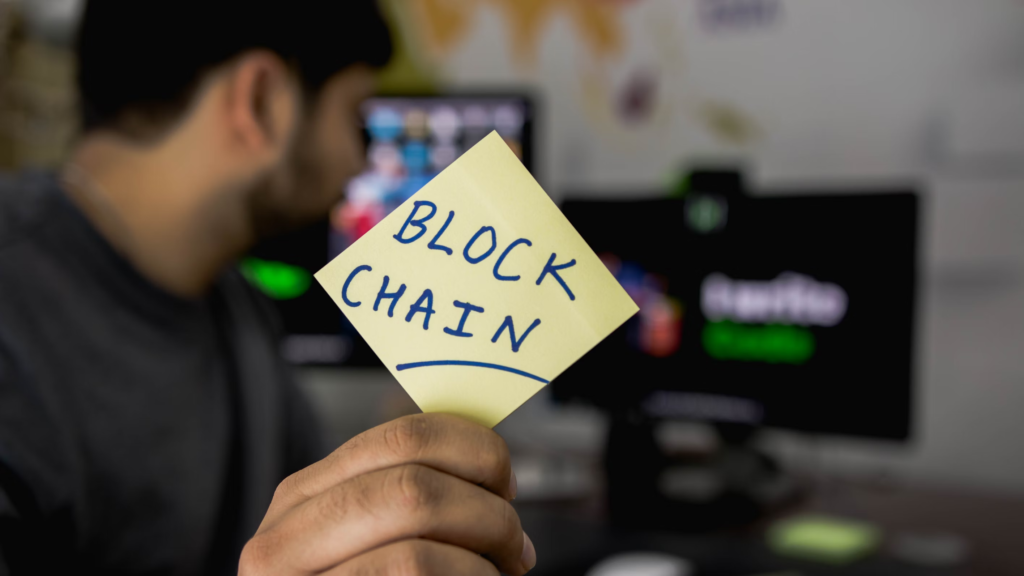 Un homme avec un post-it block chain assis devant un ordinateur