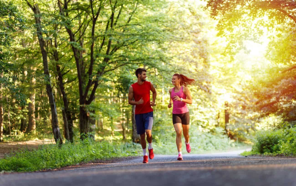Un couple de coureurs souriants sur une route bitumée dans la forêt