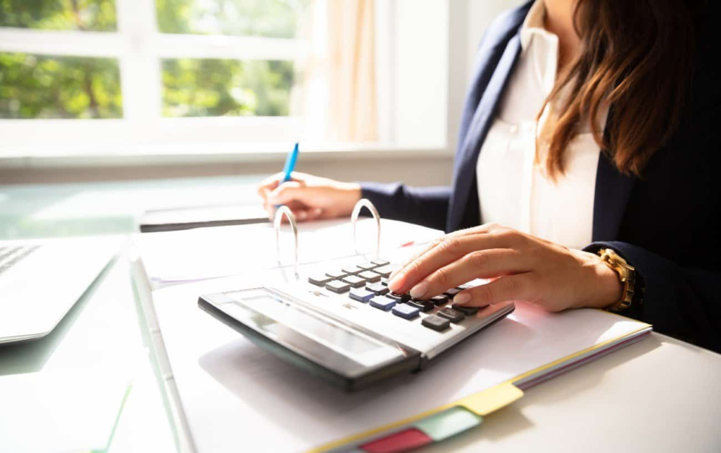 Une femme assise à un bureau fait un calcul sur sa calculatrice