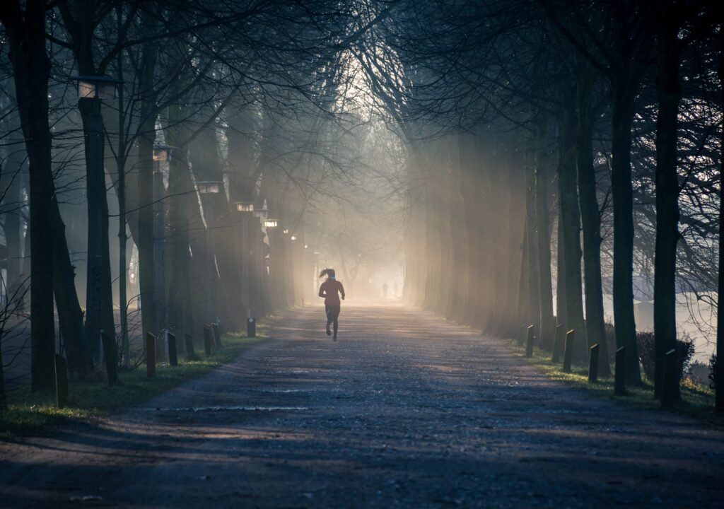 Un femme court sur une route bordée d'arbres vue de dos