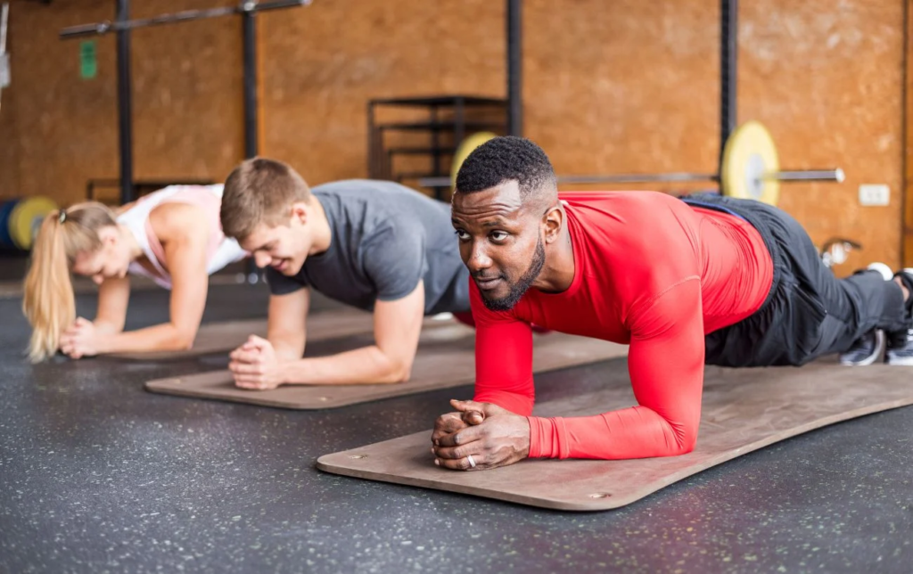 3 personnes font la planche sur un tapis dans une salle de sport