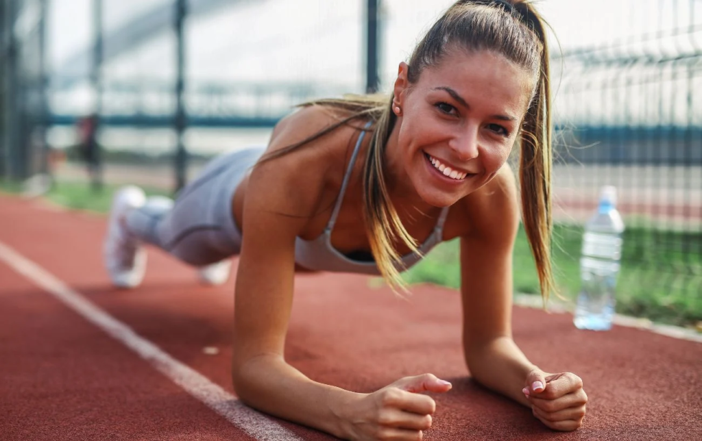 Une femme souriante fait la planche sur une piste d'athlétisme
