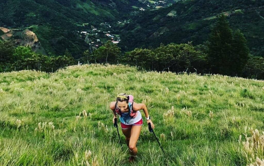 Une traileuse court dans une côte avec des bâtons de trail à la montagne