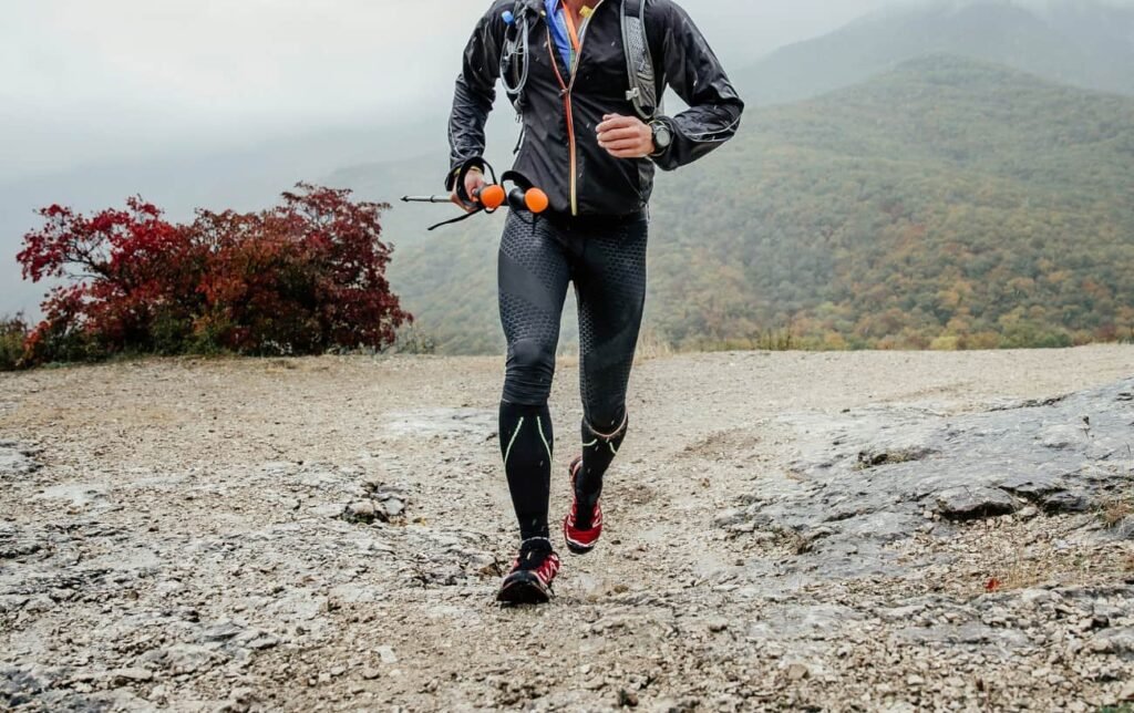 Un traileur court en côte en montagne avec des bâtons de trail